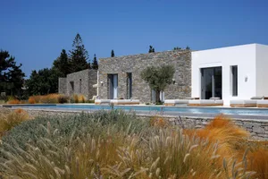 A modern minimalist house with stone walls and a white painted exterior, featuring a large swimming pool and serene garden su