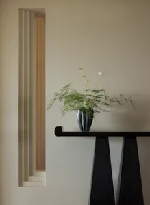 A minimalist decorative plant arrangement featuring a ceramic vase with green foliage and a small white flower, placed on a s