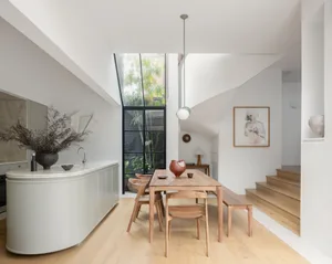 A modern kitchen and dining room with light wood flooring, a wooden dining table with chairs, and a large window.