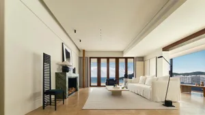 A modern living room featuring marble flooring and walls, with a large sofa, coffee table, and view of the ocean through larg