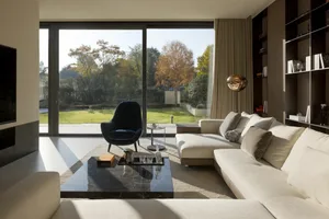 A modern living room featuring a white sectional sofa, a black marble coffee table, and a large window with a view of a garde