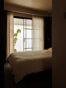A minimalist bedroom featuring textured textiles and sheer curtains, bathed in warm, natural light.