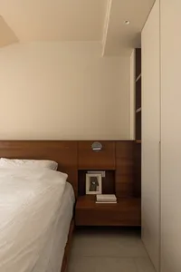 A minimalist bedroom with wooden paneling, bed, and built-in storage.