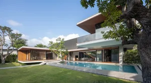 A modern residential house with glass walls, wooden accents, and a concrete foundation set against a clear blue sky.