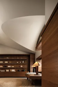 Modern living room with wooden shelves displaying books, vases, and teapots, illuminated by a wooden lamp with a dome-shaped 