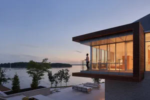 A modern residential patio overlooking a lake, featuring wood, metal, and glass elements.