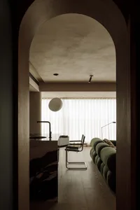 A modern living room featuring a green upholstered sofa, white curtains, and minimalist decor.