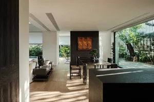 Modern living room with wooden furniture and large windows overlooking greenery.