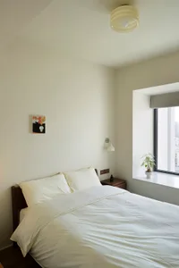 A modern minimalist bedroom featuring a white bed with simple, clean lines, accompanied by a tidy, white sheet and pillow arr