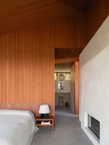 Modern minimalist bedroom featuring wood-paneled walls and concrete flooring with a cozy fireplace.