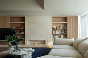 A modern minimalist living room with a beige sofa, marble coffee table, and wooden shelving.