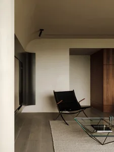 A minimalist living room featuring a black leather chair, wooden flooring, and a sleek coffee table.