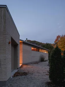 A modern residential structure featuring a concrete exterior surrounded by a gravel driveway and autumn foliage.