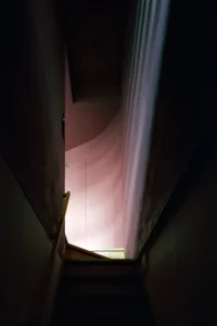 A dimly lit staircase with pink-walled walls and a light source at the bottom.