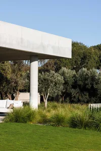 Minimalist architectural design with concrete structure, green grass, and planted trees outdoors.