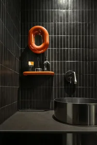 Modern minimalist bathroom featuring dark tile walls, a metal sink, and a sleek shelf with bathroom essentials.