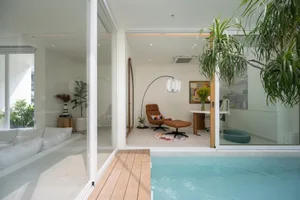 A modern minimalist living room with a glass wall, wooden flooring, and concrete elements.