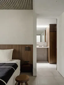 Modern bedroom with minimalist design featuring wood paneling on the headboard and walls, concrete floor, and white walls.