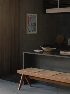 A modern entrance hall featuring a wooden bench with a woven seat, a concrete wall with a colorful abstract painting, and a c