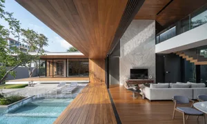 A spacious, modern residential living room with wooden flooring and a large outdoor area with a pool and lounge chairs.