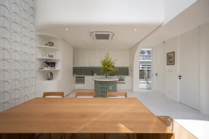 A contemporary kitchen with white tiled walls, a wooden dining table, and a central island with a green plant.