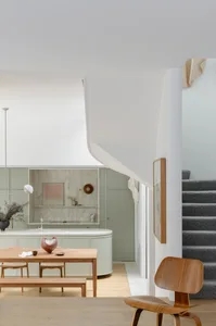 Modern minimalist kitchen with white marble countertops, light wood cabinets, and a gray carpeted staircase.