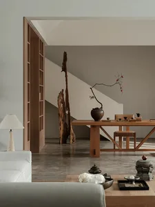 A minimalist living room with a wooden table, chairs, and coffee table, featuring an abstract wooden sculpture as a decorativ