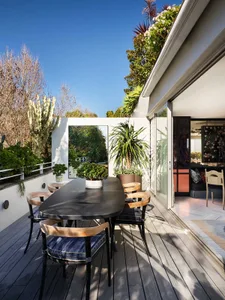 Modern, outdoor office space with a dining table, chairs, and potted plants under blue sky.