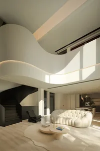 A modern indoor living room with a textured-white sofa, curved staircase, and natural light.