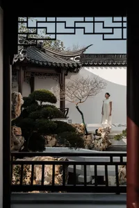 一位身穿白裙的人站在傳統花園中，周圍有石材、木造結構與玻璃元素。