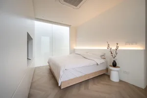 Minimalist bedroom with white bedding, wood floor, and frosted glass wall.