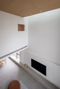 A minimalist living room with white concrete walls, wood ceiling, and a sleek fireplace.