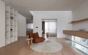 A modern minimalist living space featuring a leather armchair, round rug, and wooden coffee table.