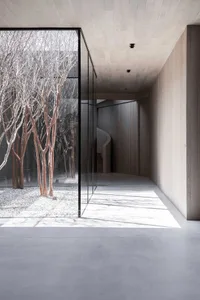 A modern architectural space with concrete walls, a spiral staircase, and a view of a snowy courtyard filled with trees.