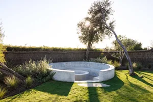 Circular concrete seating area in a modern garden with lush greenery and a sunlit sky.