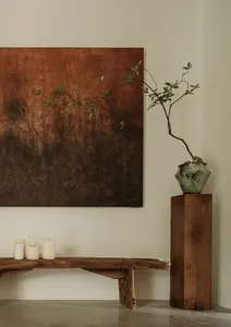 Modern interior design featuring wooden bench, stone vase, and metal vase with greenery.