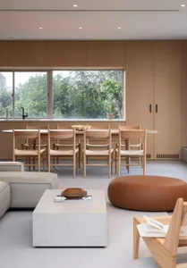 A modern living and dining space featuring wooden furniture and concrete floors, with a large window overlooking greenery.