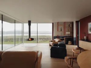 Modern living room featuring timber flooring, furniture, and windows overlooking a scenic landscape.