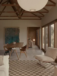 A modern living room with a wooden table, chairs, and floor lamp, featuring a large window and exposed wooden beams on the ce