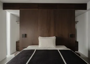 A modern minimalist bedroom with a wooden panel wall, white bedding, and a black and white striped blanket.