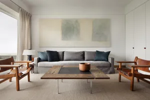 A minimalist living room with a wooden coffee table, grey sofa, and wooden chairs.