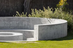 Circular, minimalist seating area made of concrete with greenery surrounding it.