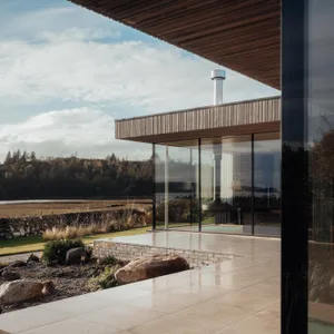 A modern residential exterior featuring glass windows, stone accents, and natural wood elements.