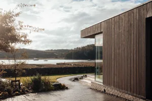 Modern residential exterior featuring wooden panels and glass windows overlooking a scenic lakeside view.