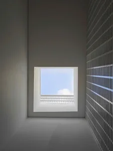 A minimalist, metallic window frame with a steel panel design, set in a white, industrial-style room with a grid-like wall pa