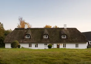 A quaint, white-washed cottage with a thatched roof surrounded by lush green grass.