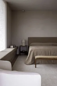 Minimalist bedroom featuring beige and wooden furniture, linen sheets, and a large window