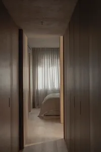Minimalist bedroom with neutral-toned textiles and light filtering through sheer curtains.