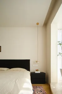 Minimalist bedroom with white walls, wooden furniture, and a bed covered in white bedding.