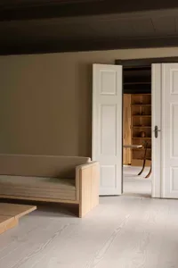 A minimalist living room with a wooden sofa and an open doorway into a dining area.